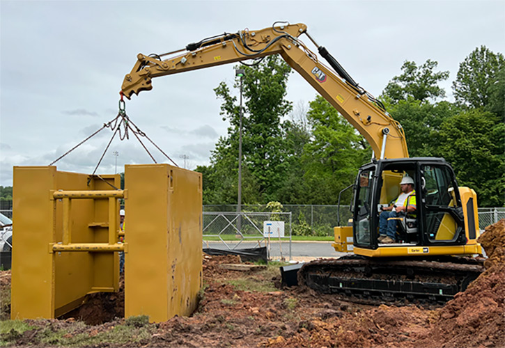Worker lowering a trench box into hole